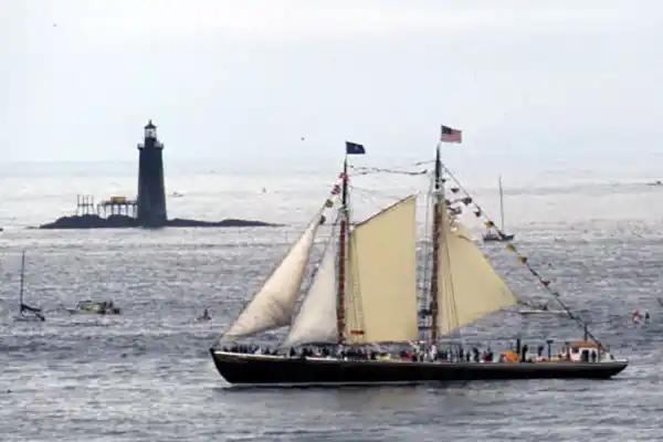 Sail boat crossing in front of lighthouse in coastal Maine