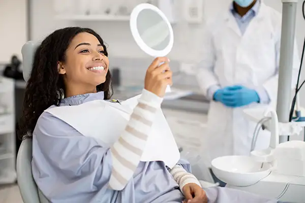 Smiling dental patient sitting in dental exam chair and looking in mirror